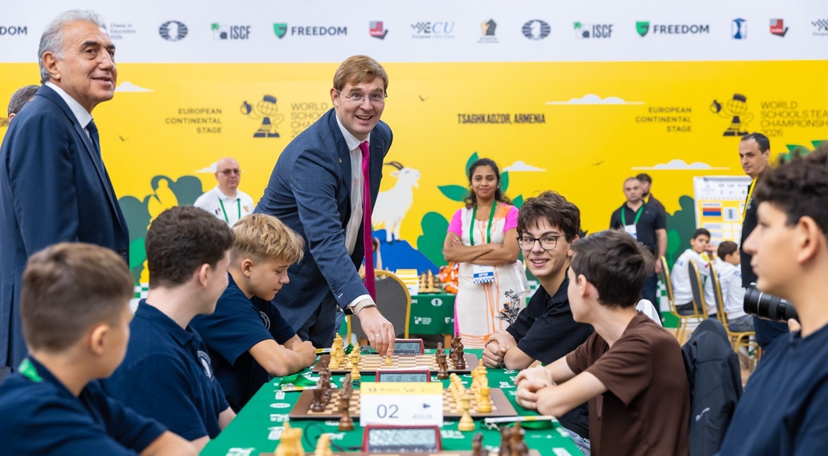 Timur Turlov俯身在赛场棋盘上走棋，几名学生围坐棋盘两侧。